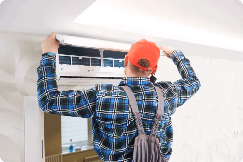 HVAC technician maintaining wall-mounted AC unit.