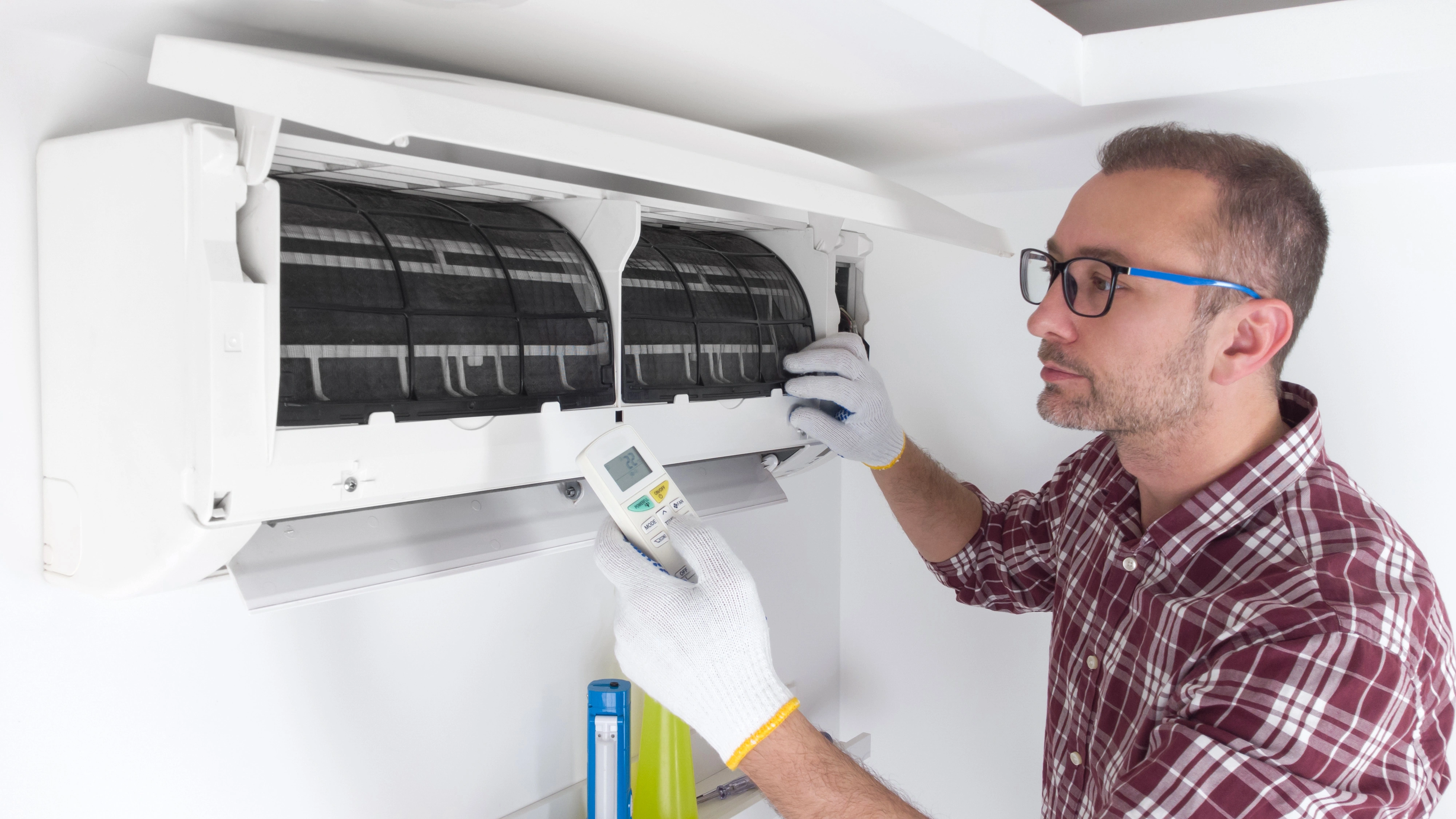 Cartoon of a smiling technician in a red cap and blue shirt, kneeling beside an air conditioning unit
