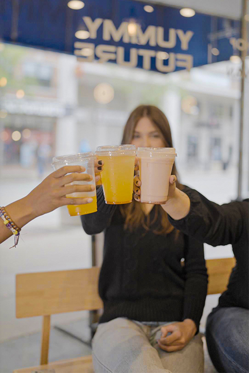 A couple of people sitting on a bench with drinks.