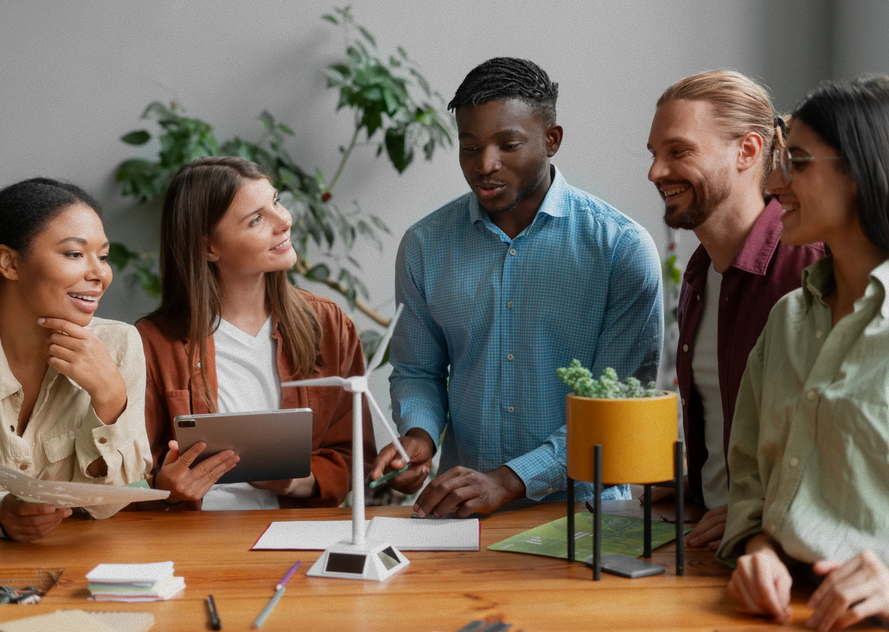 Students gathered around a table listening to a peer explain part of their group assignment.