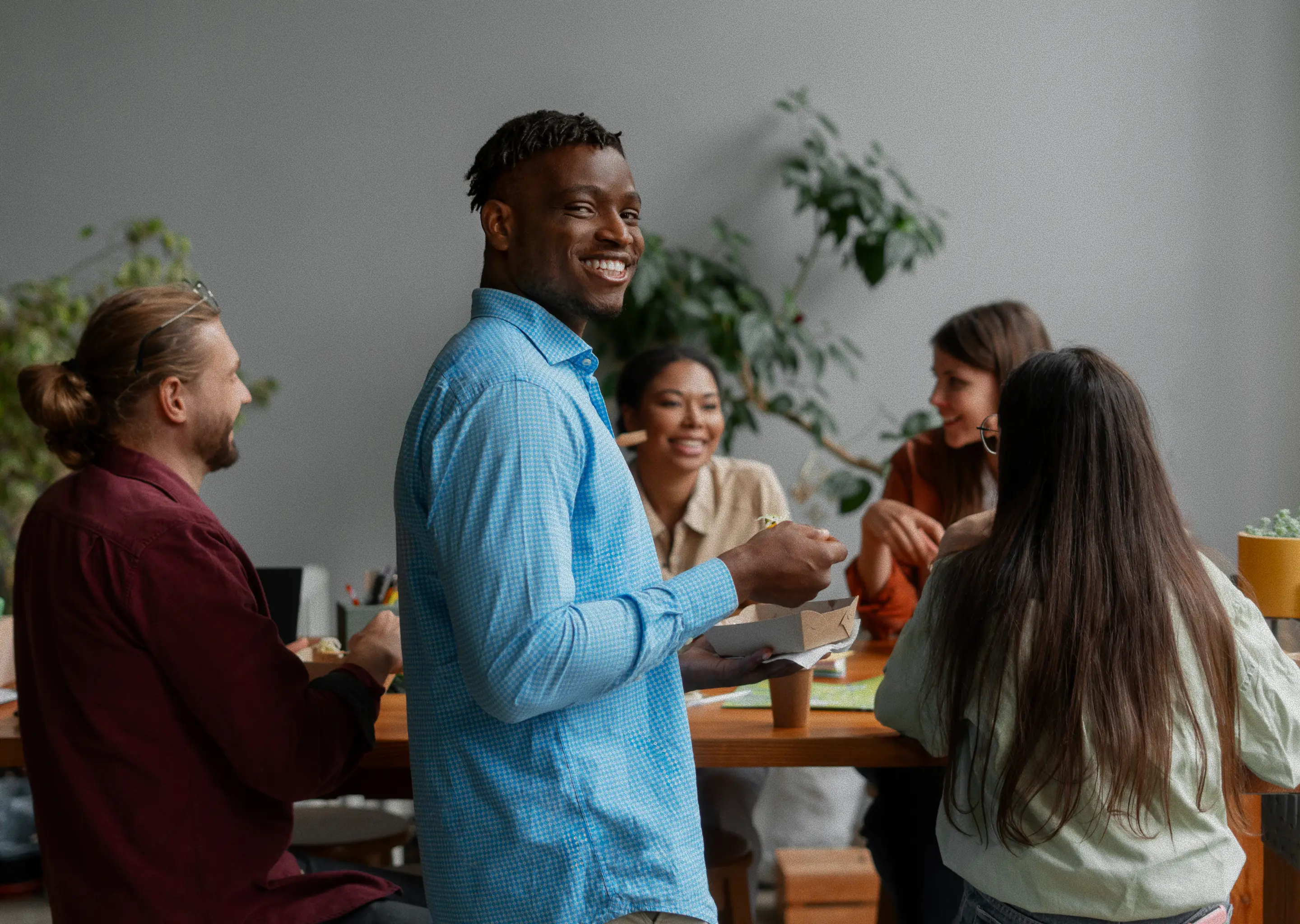 Student smiling while eating lunch as classmates chat around the table.