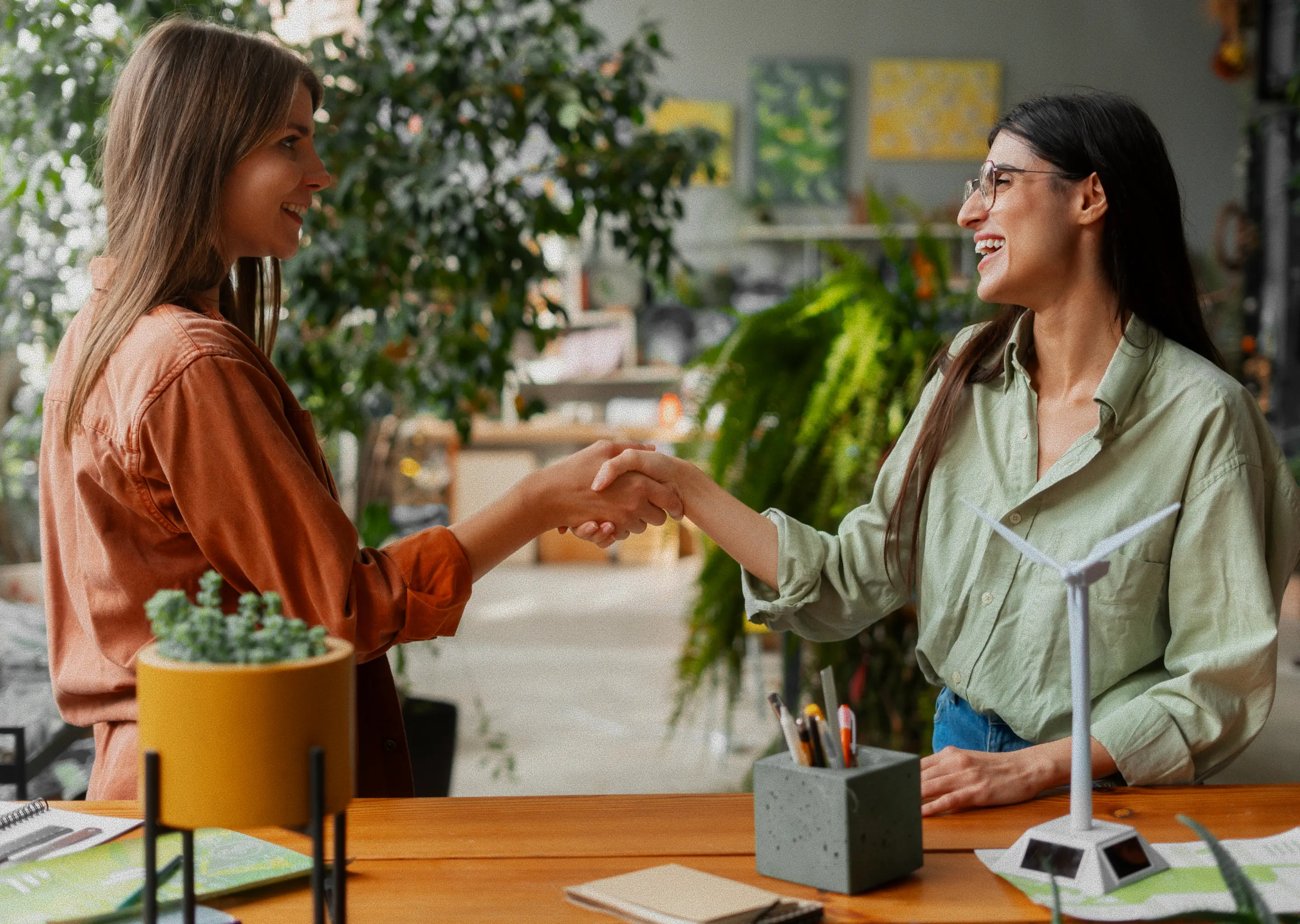 Two students shaking hands across a table, showing teamwork and agreement.