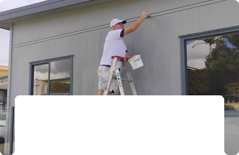 This shows a picture of Glenn on a ladder painting a house in Northland
