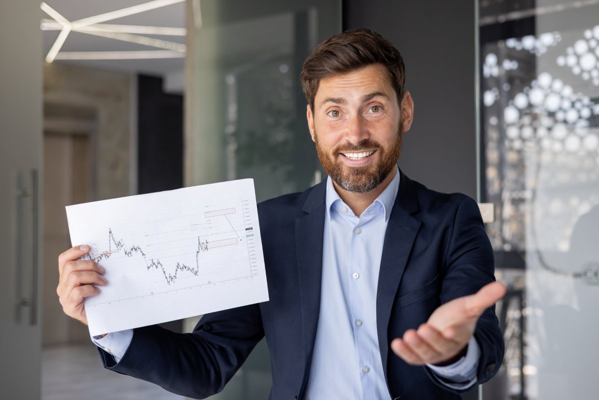 Smiling, professional businessman holding a financial graph, gesturing an inviting hand, indicating growth in a modern office setting