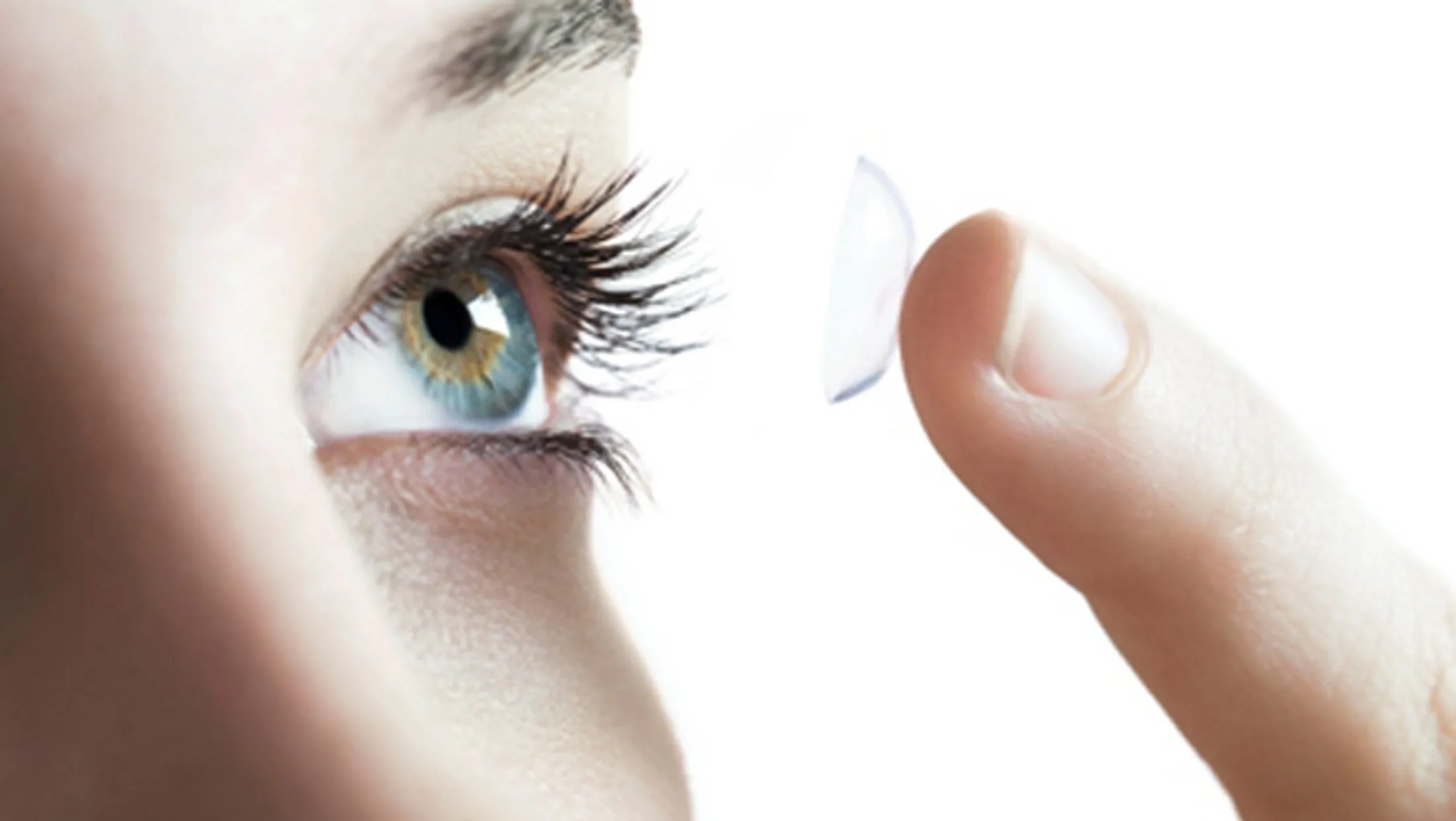 Close-up of blue eye with contact lens being inserted by finger