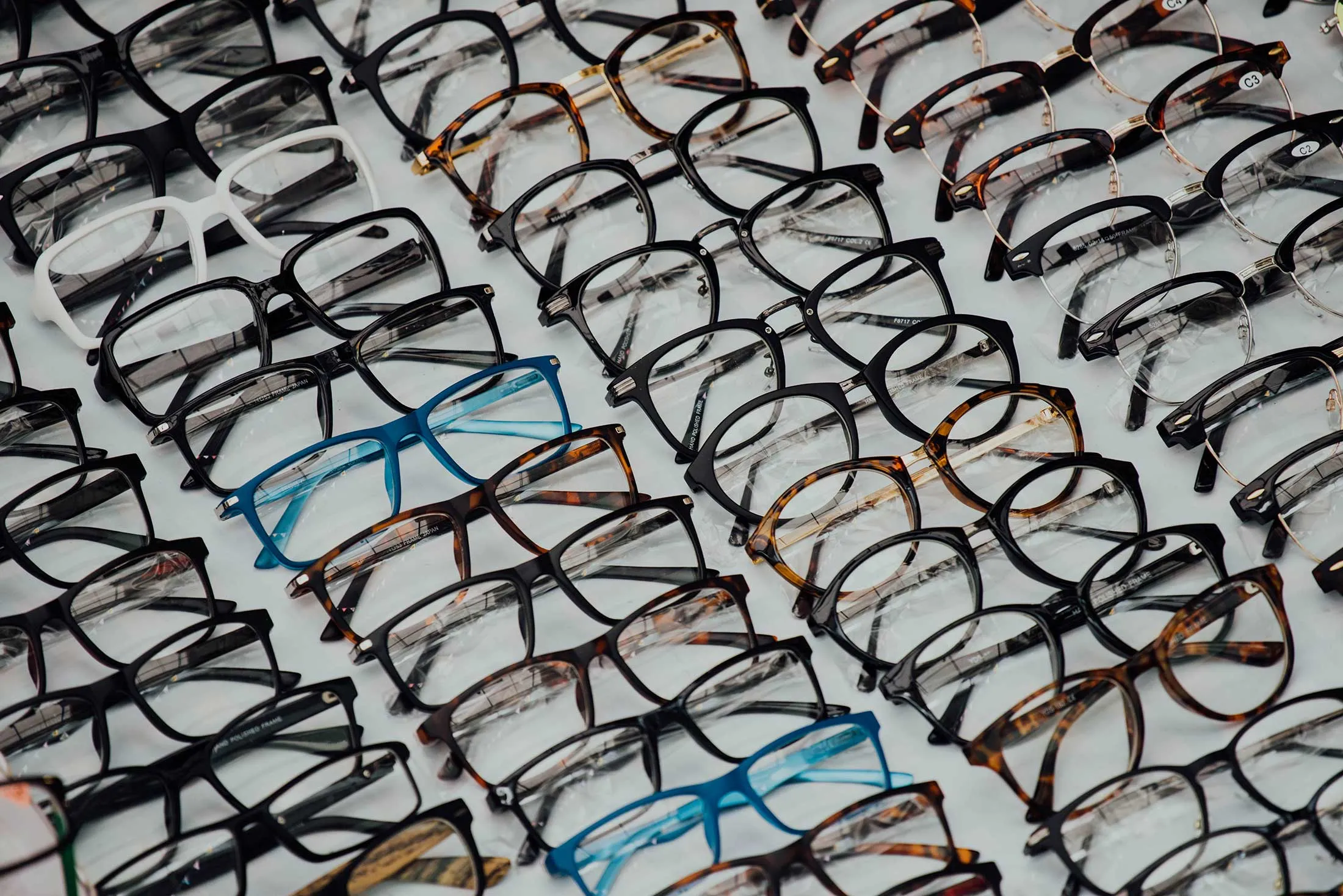 Many eyeglasses in various colors and styles neatly arranged on a white background