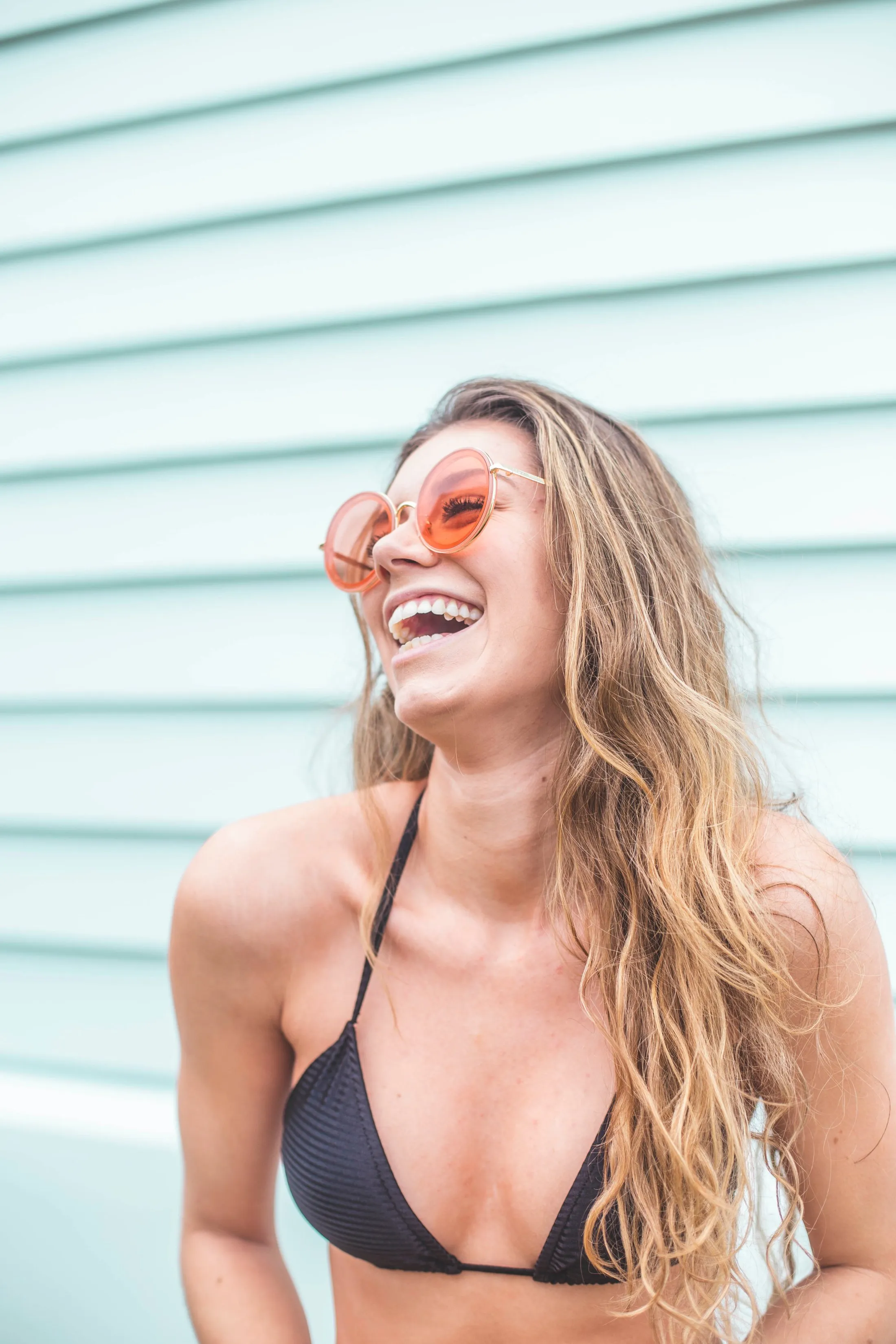Woman in orange sunglasses laughing joyfully by striped wall