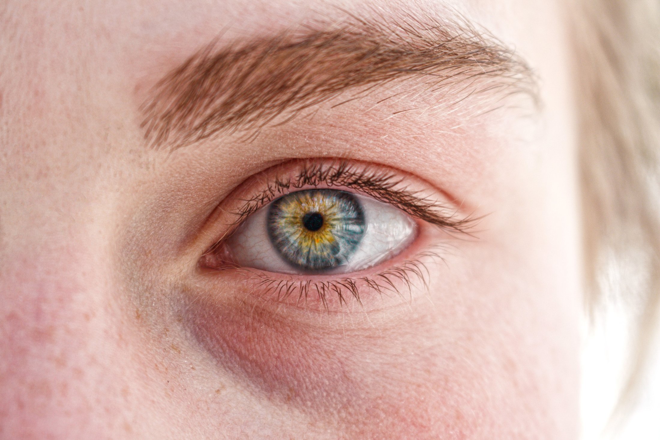 Extreme close-up of a blue-green and yellow human eye with detailed iris