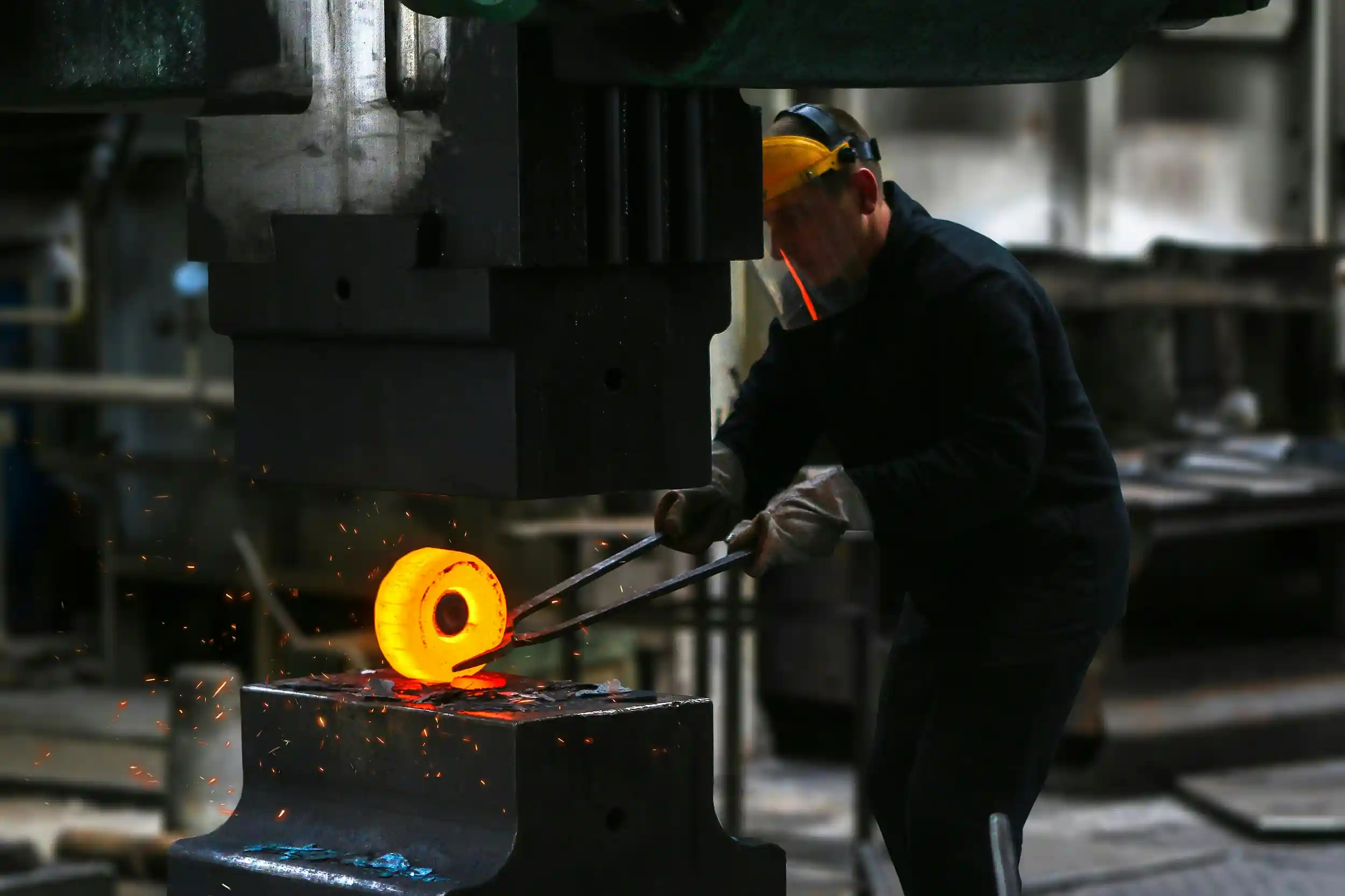 A man working with hot metal on an open-die forging press