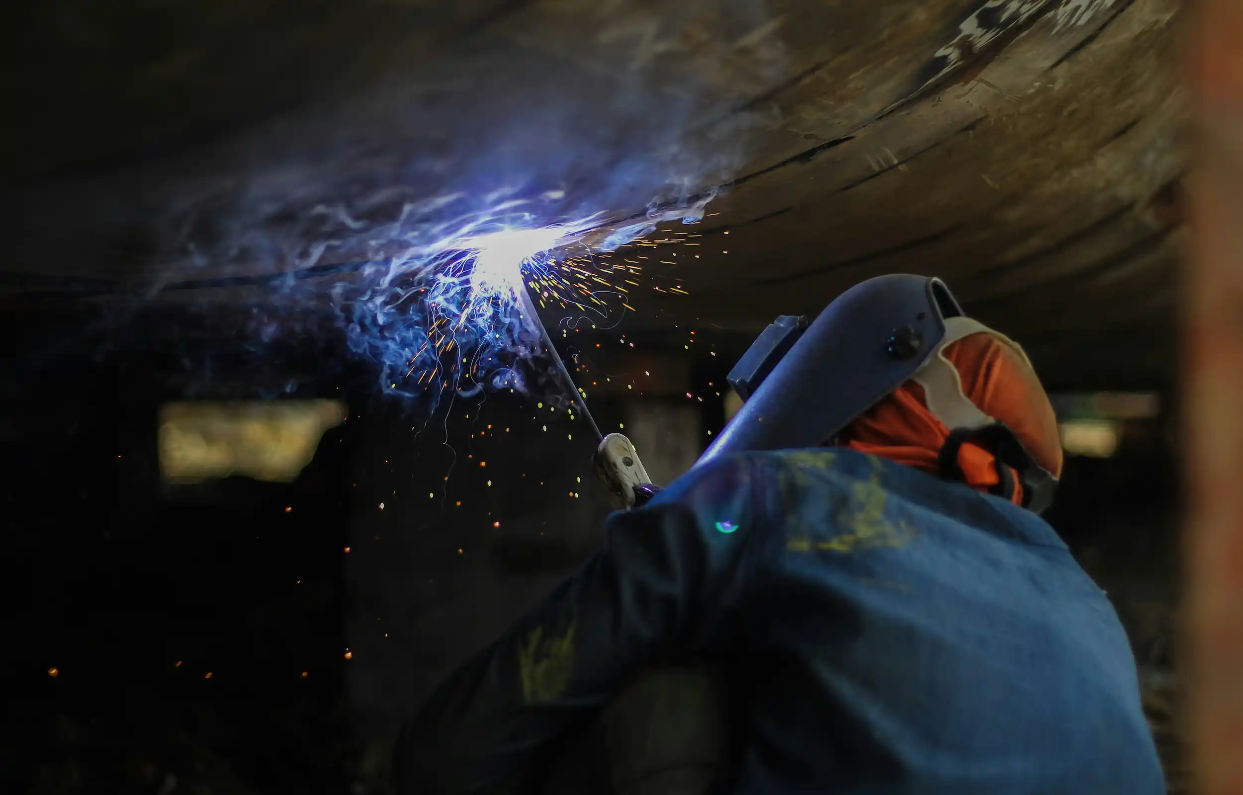 A man stick welding on the underside of a large structure
