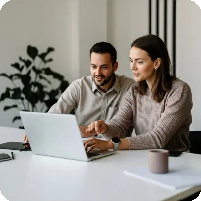 Man and woman collaborate at a table, smiling as they review a laptop screen, suggesting teamwork and support.