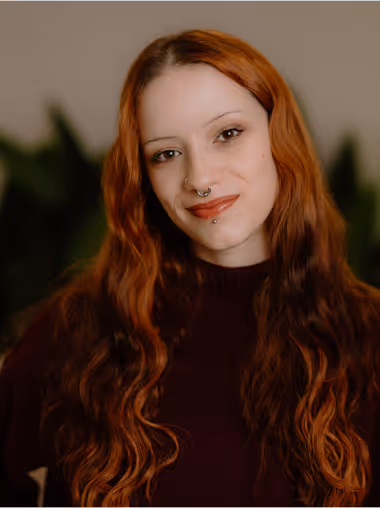 Young woman with long wavy red hair, wearing a dark sweater and smiling softly at the camera.