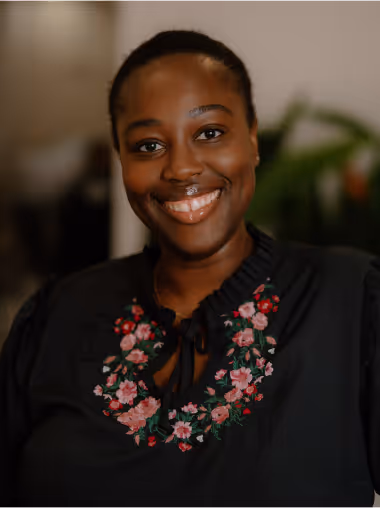Smiling woman wearing a black top embroidered with pink and red flowers.
