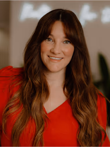 Smiling woman with long brown hair wearing a red top against a blurred background.