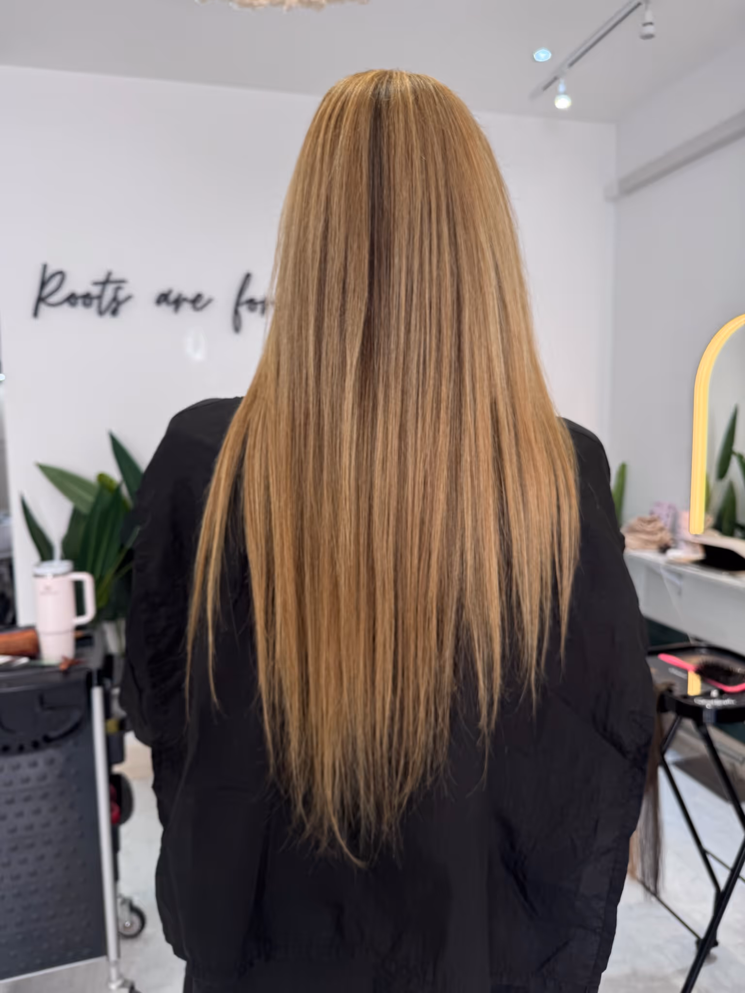 Person with long, straight, highlighted blonde hair viewed from the back in a salon setting.