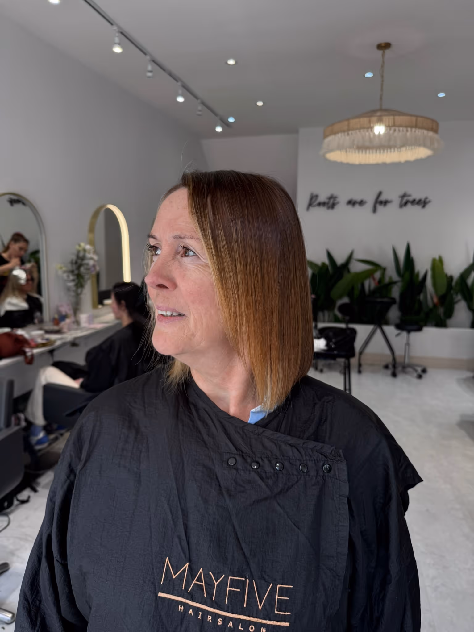 Woman with straight, shoulder-length brown hair sitting in a hair salon wearing a black salon cape.