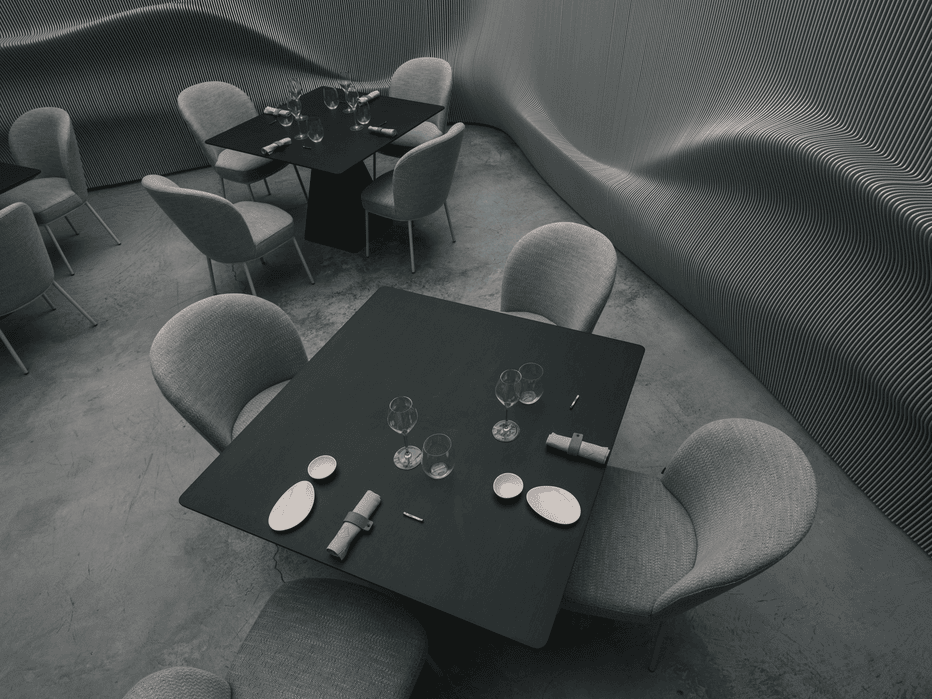 Modern dining area with square black tables set with glassware and napkins, surrounded by curved upholstered chairs and a textured wavy wall bench.