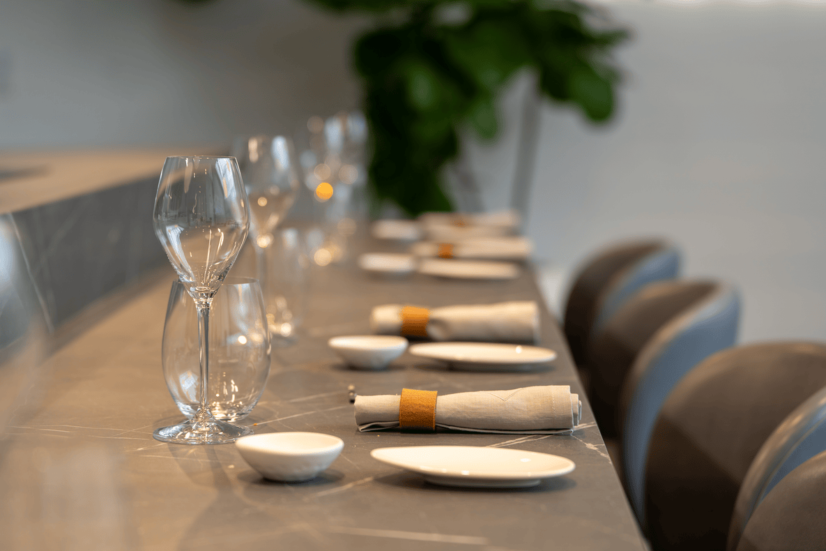 Close-up of a modern dining table set with white plates, rolled gray napkins with brown holders, glassware, and small white bowls.