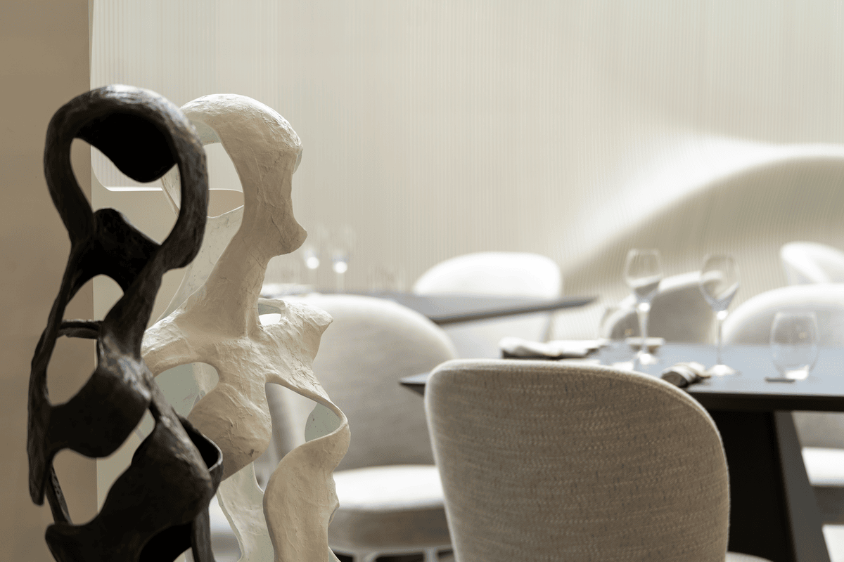 Abstract black and white sculptures resembling human forms in a softly lit dining area with blurred tables and chairs.