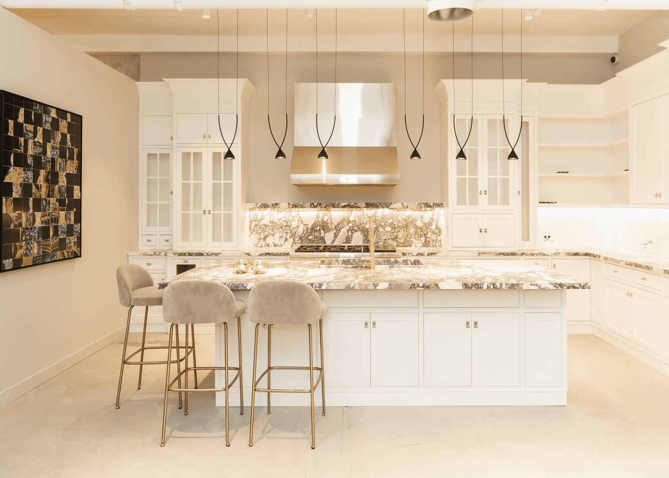 Modern kitchen with white cabinetry, marble countertops, a large island with three beige velvet bar stools, and black pendant lights.