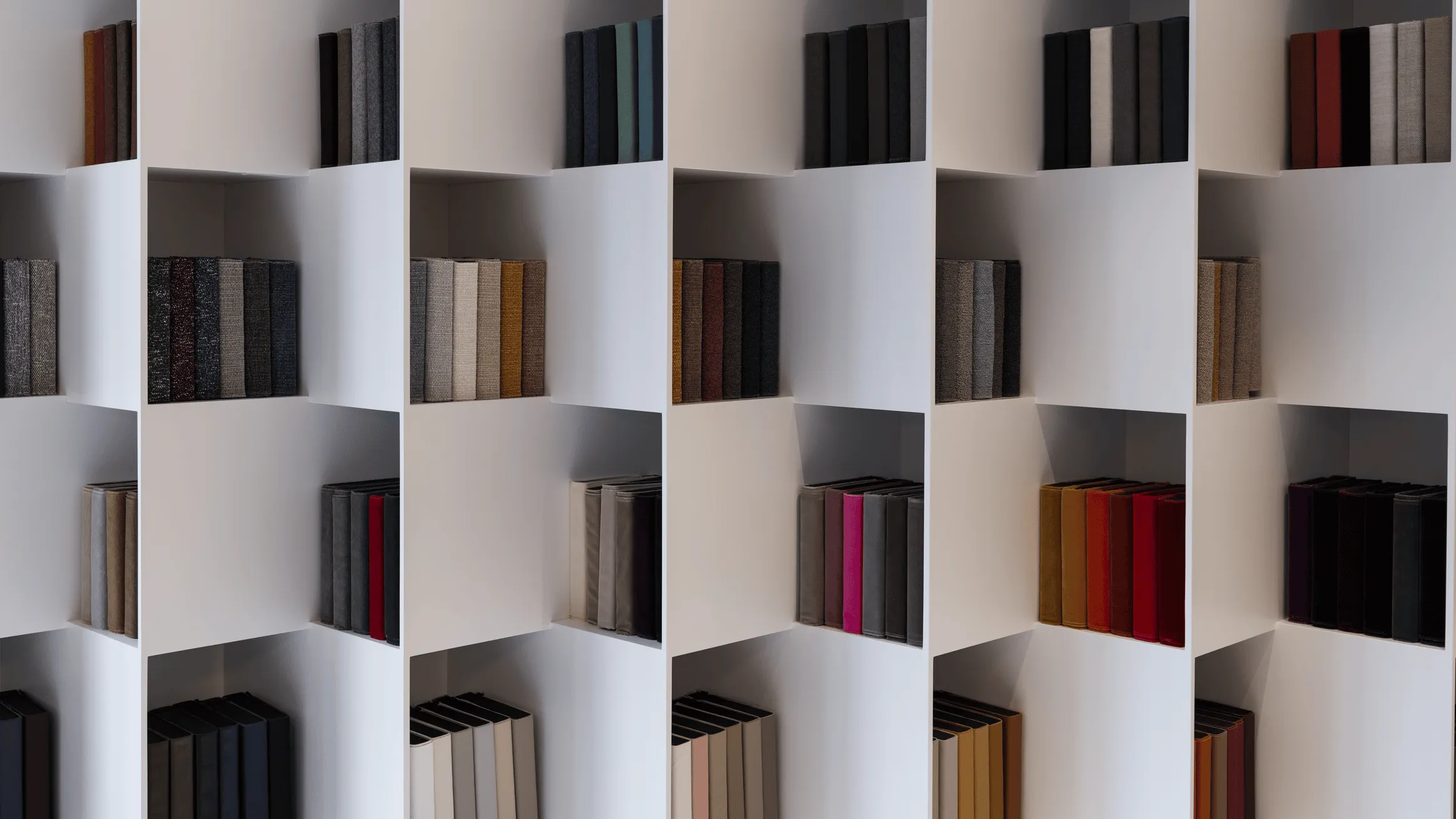 White bookshelf with multiple cubby holes filled with vertically arranged fabric-bound books in various neutral and warm colors.