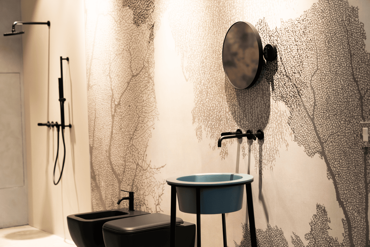 Modern bathroom with black fixtures, a round wall-mounted mirror, and a blue freestanding sink against a wall decorated with intricate tree branch patterns.