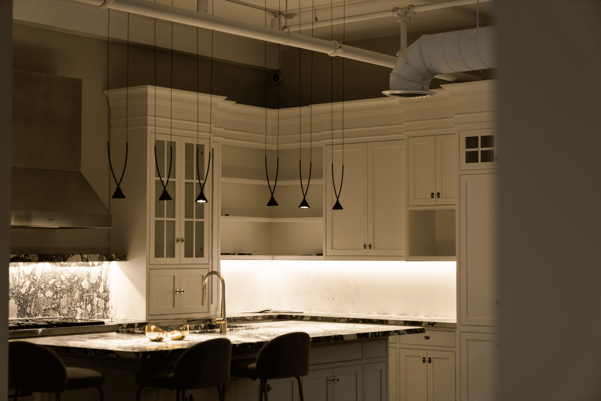 Modern kitchen with white cabinets, marble countertops, hanging pendant lights, and a stainless steel range hood.