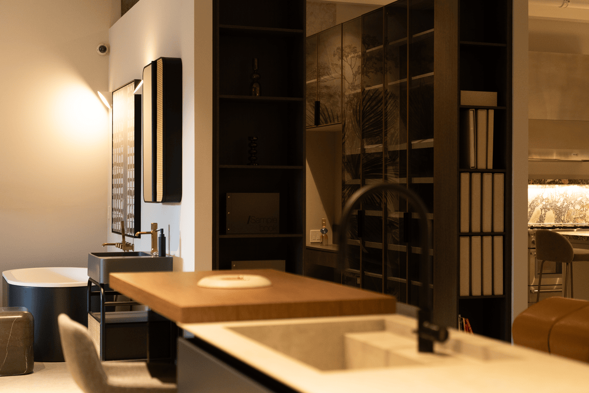 Modern bathroom with a black freestanding bathtub, gray sink, wooden countertop, and shelves with books and decor.