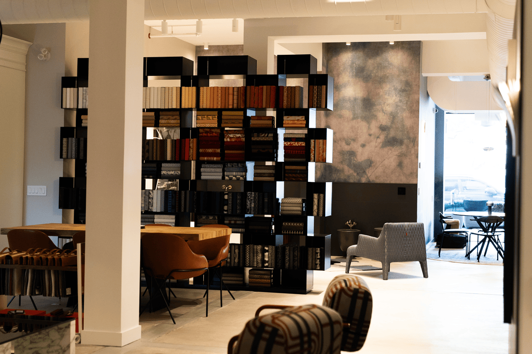 Modern interior with a geometric black bookshelf filled with folded fabrics, leather chairs, and a large textured wall panel.