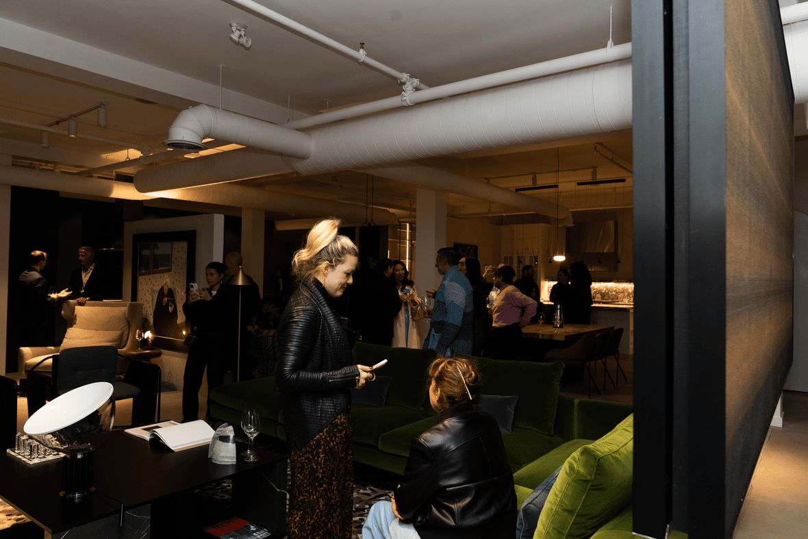 People socializing in a modern indoor lounge with green velvet couches, ambient lighting, and exposed white ceiling pipes.