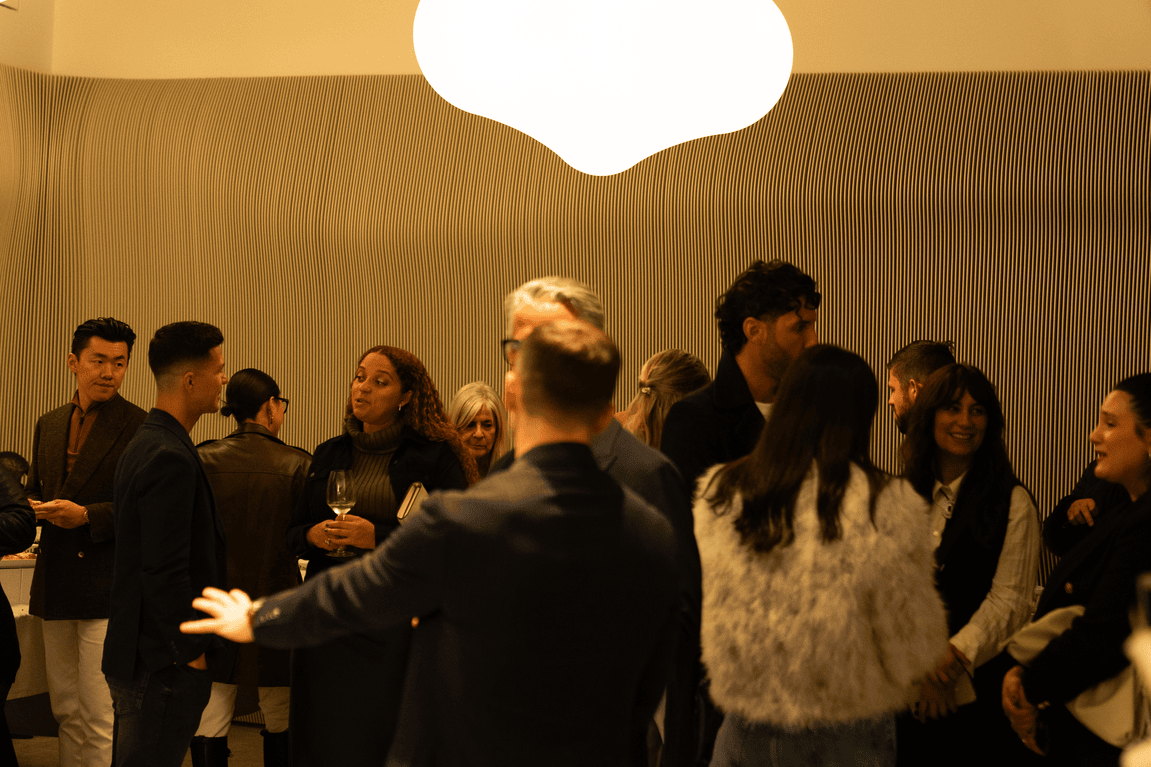 Group of people engaged in conversation at an indoor social event with warm lighting and a wavy striped wall in the background.