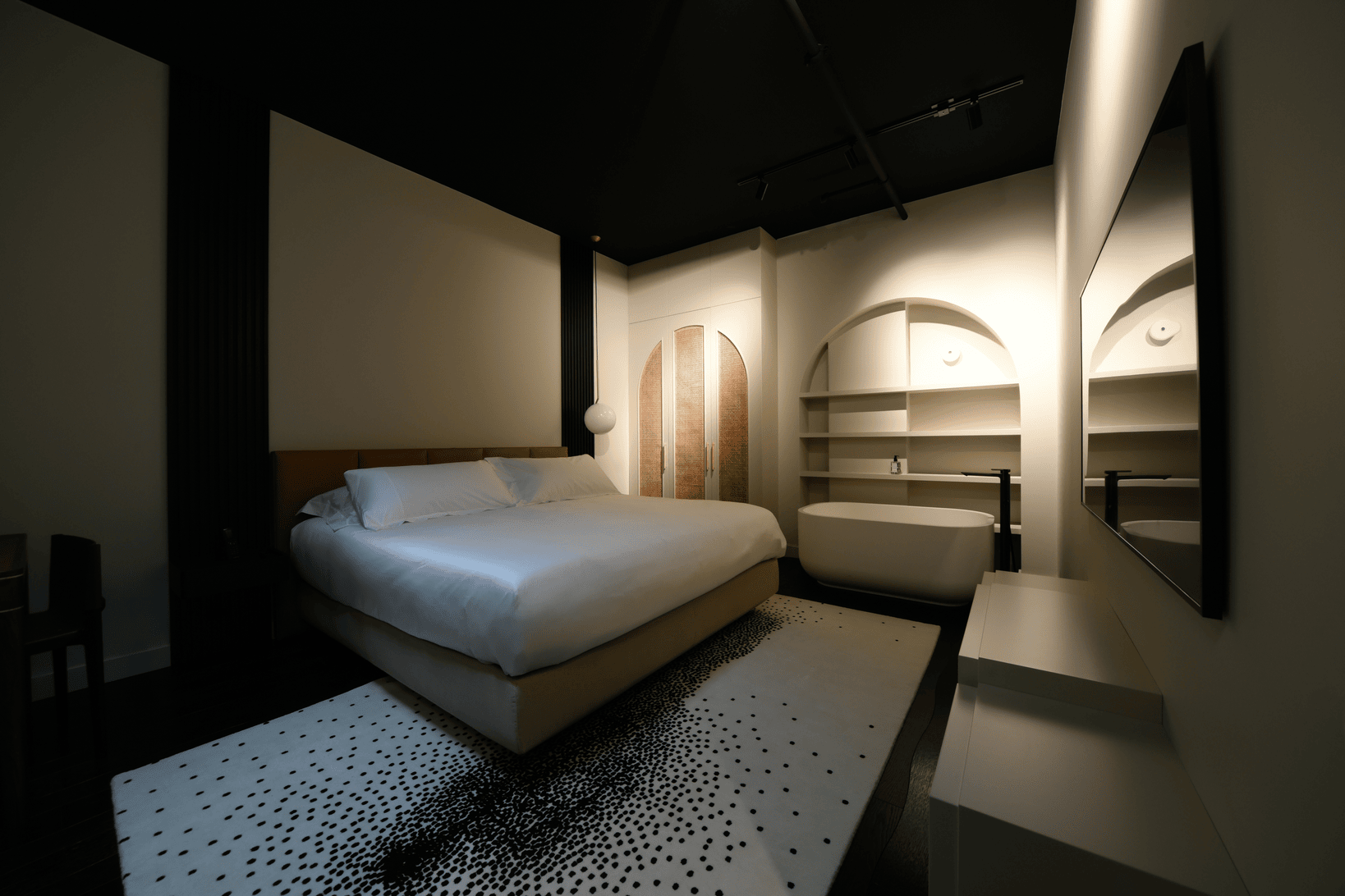 Modern bedroom with large bed, white bedding, black ceiling, patterned rug, and white bathtub under arched shelving.