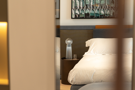 Cozy bedroom with a white bed, a bedside table holding a modern lamp, and abstract artwork on the wall.