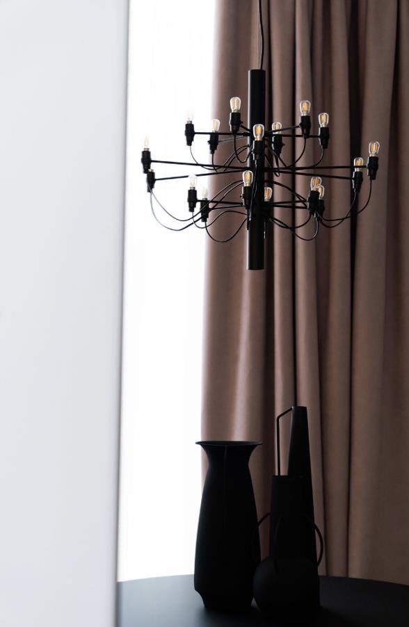 Modern black chandelier with exposed bulbs hanging above a round table with black decorative vases, set against brown curtains.