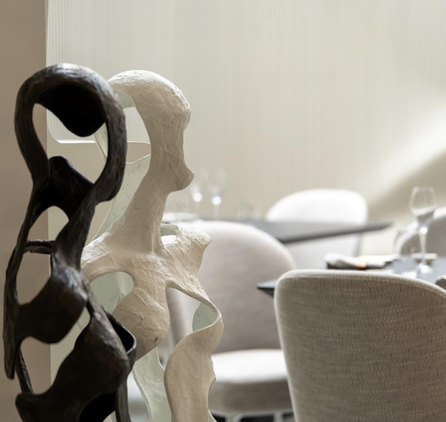 Abstract black and white sculptures in front of blurred dining chairs and tables in a softly lit room.