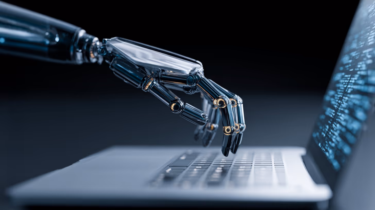 Robotic metallic hand typing on a laptop keyboard with code displayed on the screen.
