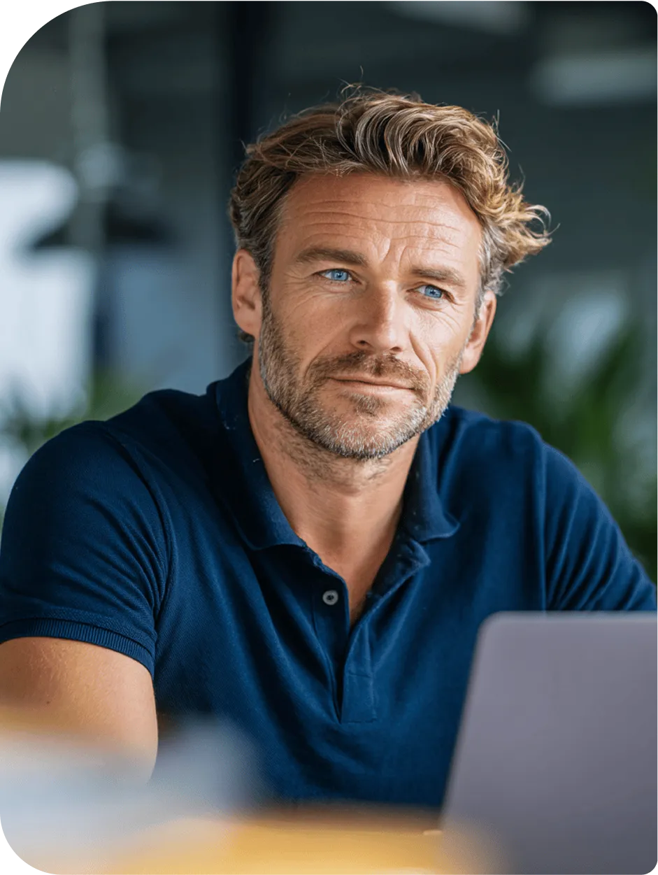 A thoughtful middle-aged man with blue eyes and a blue polo shirt, sitting with a laptop