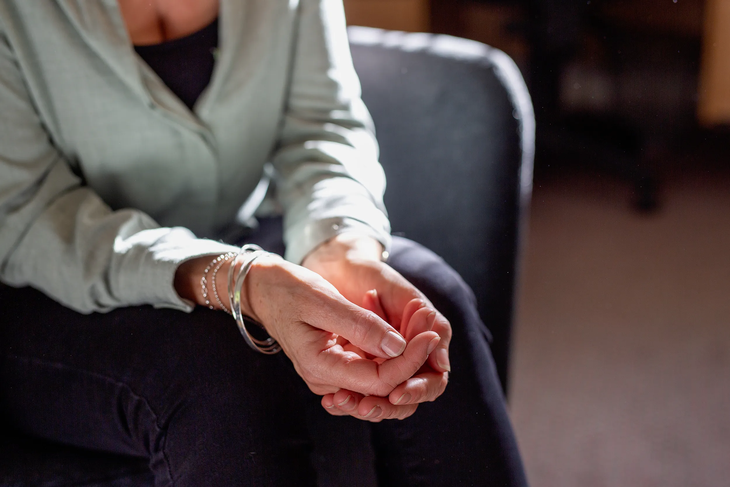 A close up of a females hands resting on their knees while sat in a chair. 