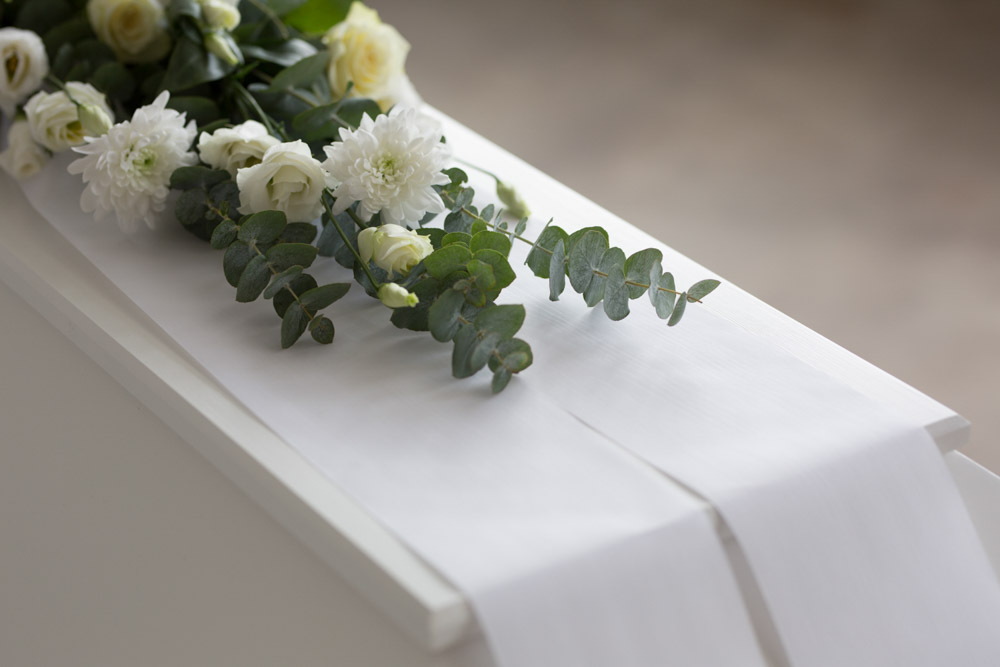 en hvit kiste med hvite blomster og bånd på