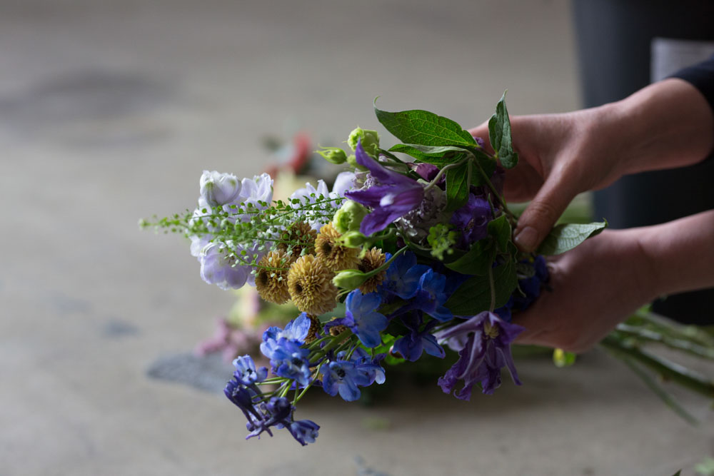 en bukett med lilla, gule og grønne blomster med hender som holder den