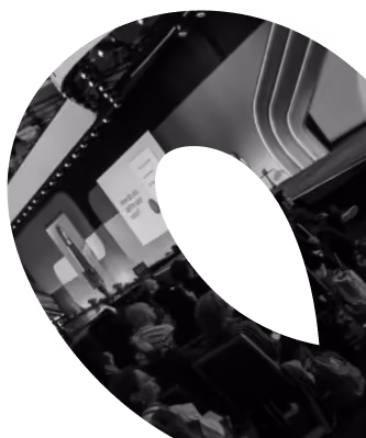 Audience seated and facing a stage with projected slides and a presenter in a large conference or seminar setting.