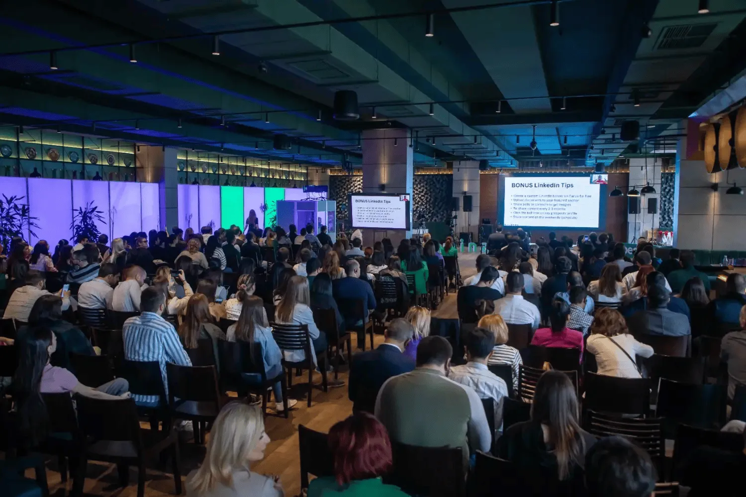 Large audience seated in rows watching a presentation in a modern conference room with two screens showing LinkedIn Tips.