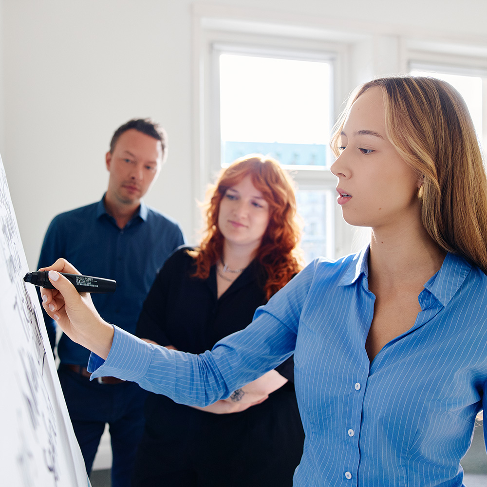 Three people discussing something on a whiteboard.