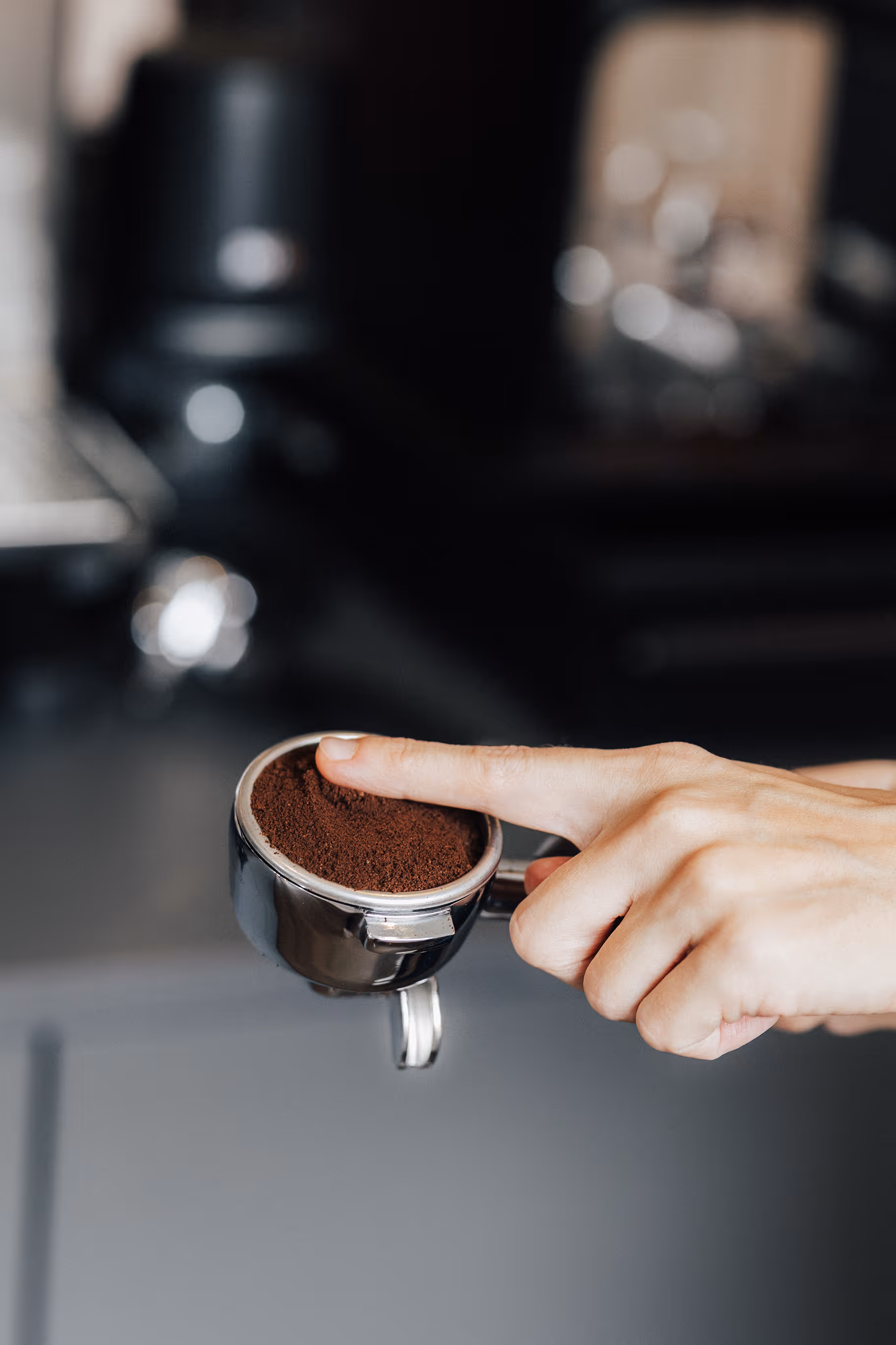 Hand drückt mit dem Finger Kaffeepulver in einem Siebträger.