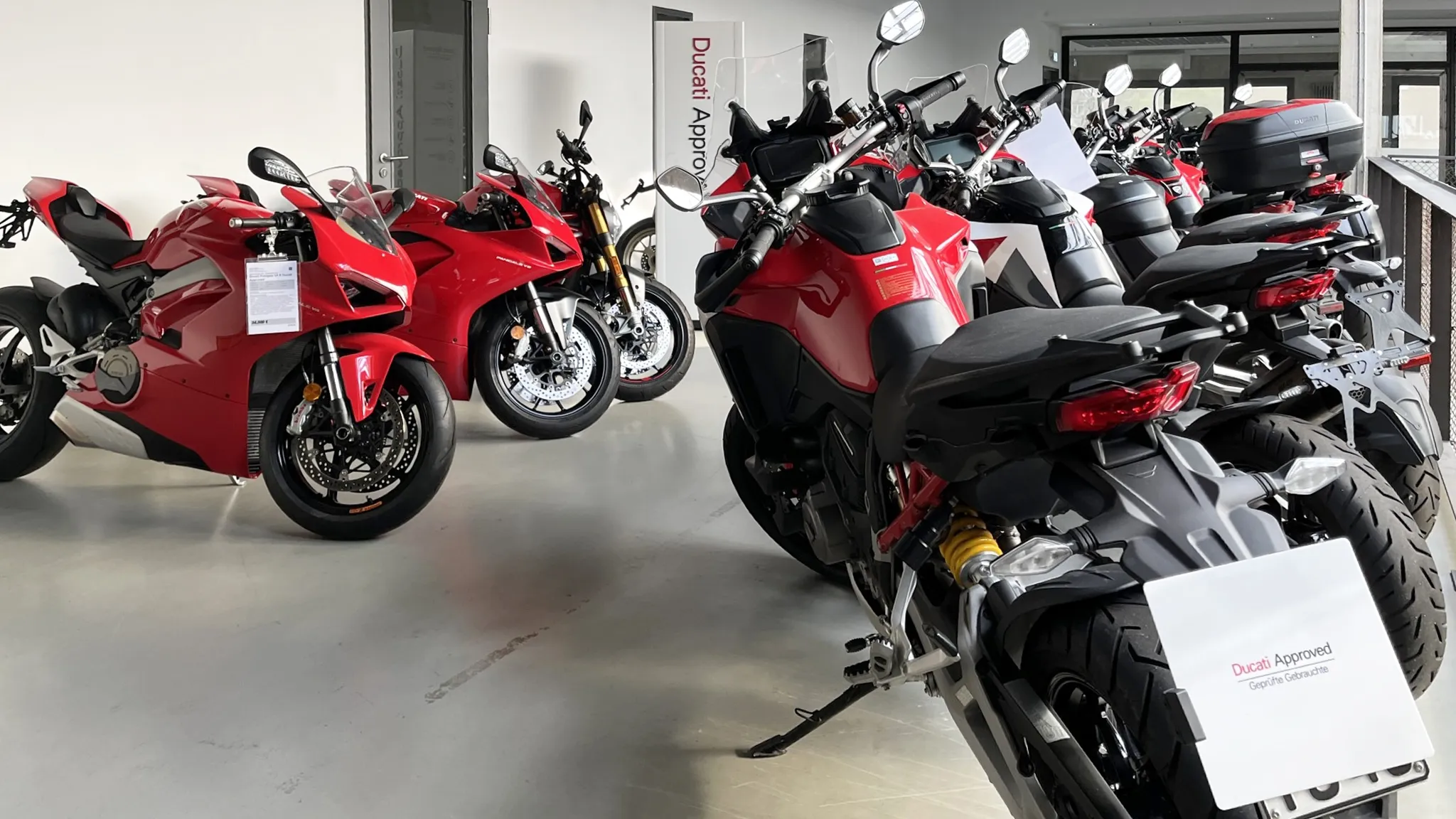 Mehrere rote Ducati Motorräder in einer Ausstellungshalle, darunter Sport- und Touringmodelle, mit Ducati Approved Schild für geprüfte Gebrauchtmotorräder.