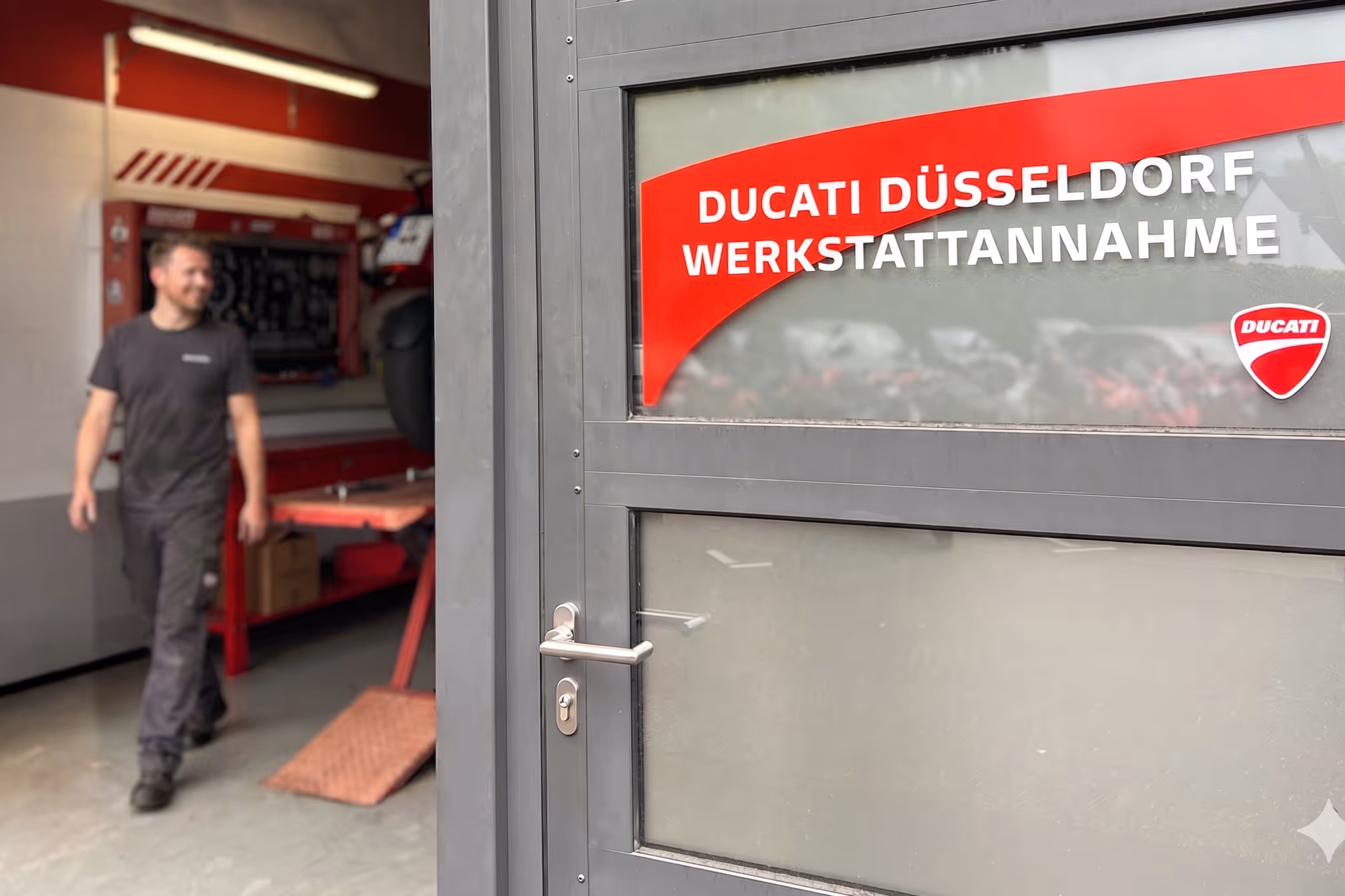Türschild Ducati Düsseldorf Werkstattannahme mit einem Mann, der in Werkstattbereich geht.