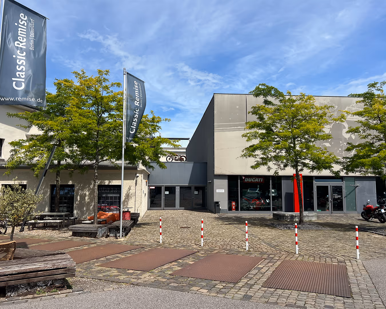 Gebäudeeingang von Classic Remise Berlin Düsseldorf mit Ducati-Schaufenster und Fahnen im Innenhof.