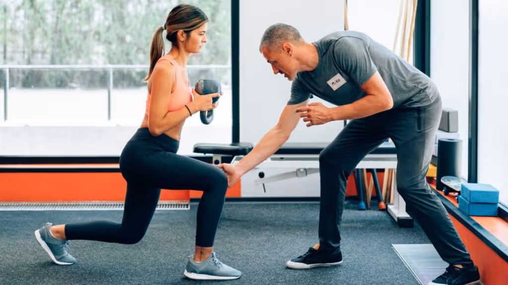 Frau wird von Personal Trainer korrigiert.