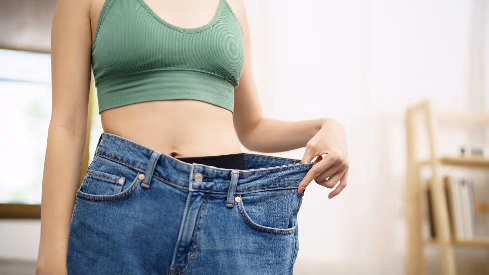 Frau hat eine viel zu große Hose an und präsentiert ihre Abnahme.