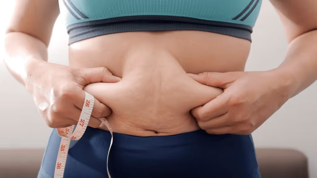 Frau misst ihren Bauchumfang und hält Bauchfett fest – Symbolbild für viszerales Fett und Abnehmen im Bauchbereich